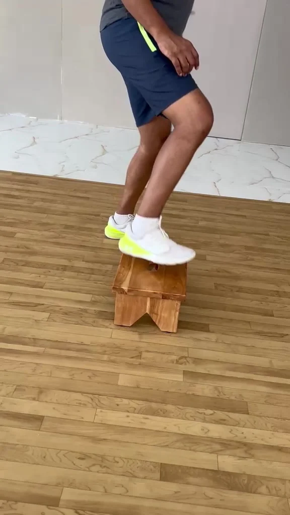 Both feet on a wooden step stool with knees bent, seen from the side