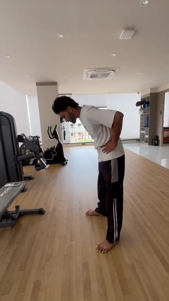 Barefoot man bends forward from the waist with both hands supporting his lower back