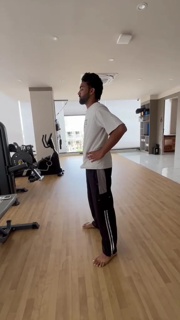 Barefoot man stands side-on in a gym with both hands pressed against his lower back