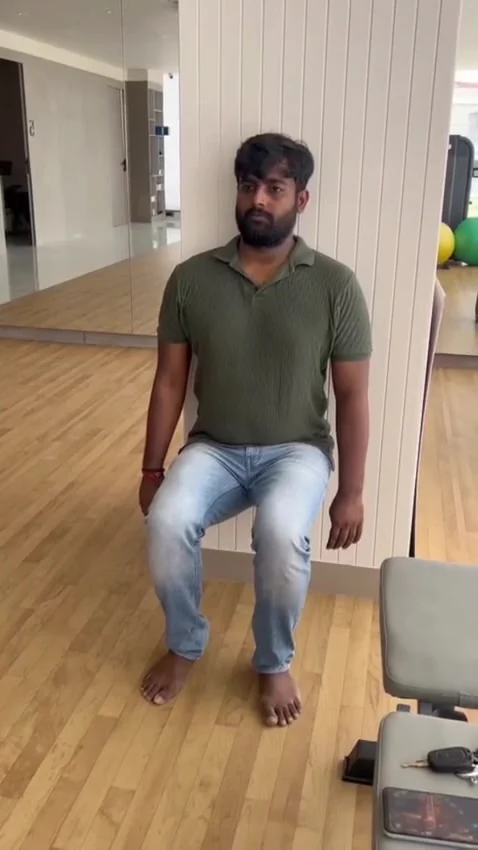 Bearded man in olive polo holds a squat with his back against a white slatted wall
