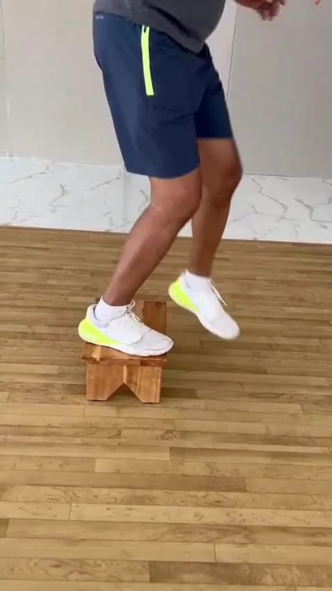 One foot on a wooden stool, the other lifted in the air beside it