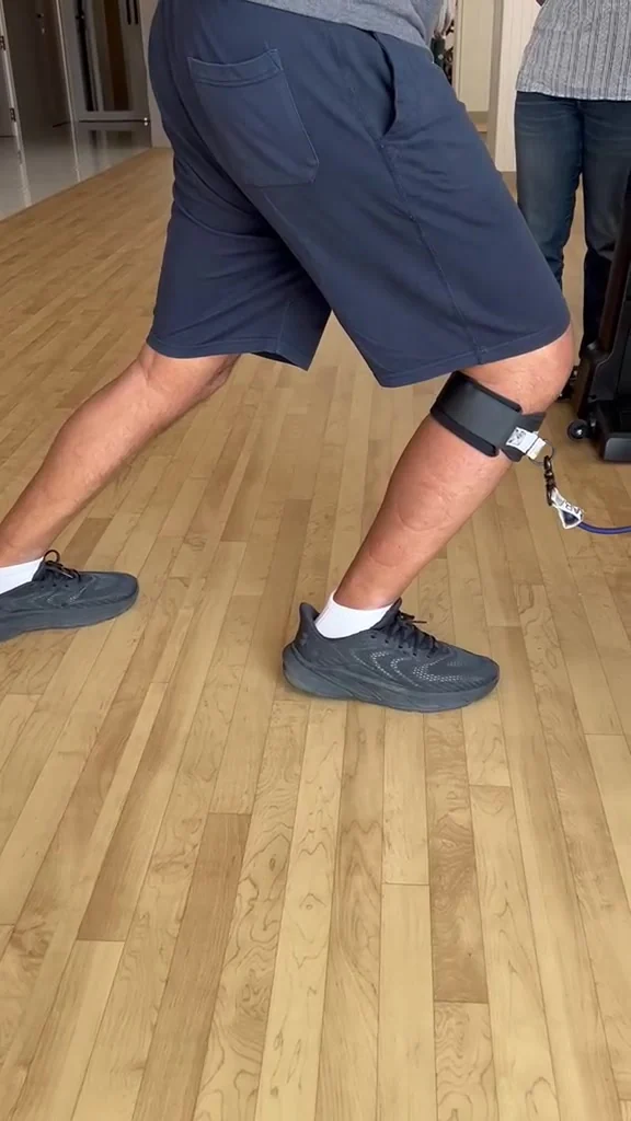 Legs in shorts and trainers mid-step, with a cuff and cord fastened around the upper calf below the knee.