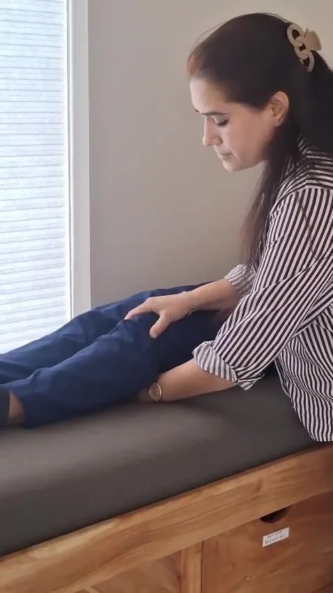 Woman in striped shirt rests a hand on the knee of someone lying on a couch