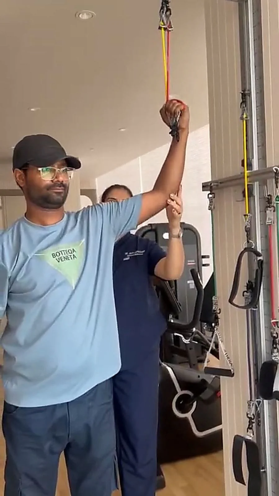Therapist supporting a patient's arm during an overhead pull at the resistance band wall