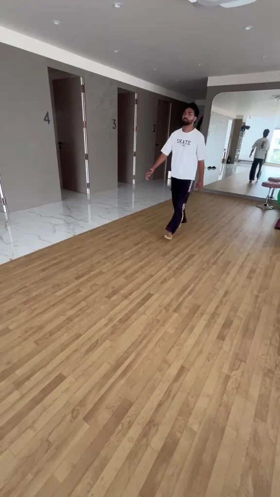 Bearded man in a white tee walks toward the camera across a studio floor
