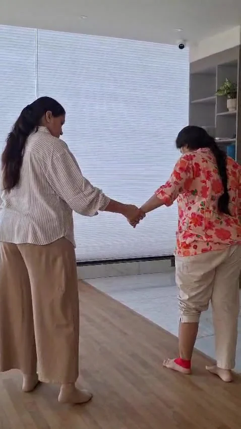 Woman in a floral kurta leaning forward onto her front foot while a second woman holds her hand at arm's length beside her
