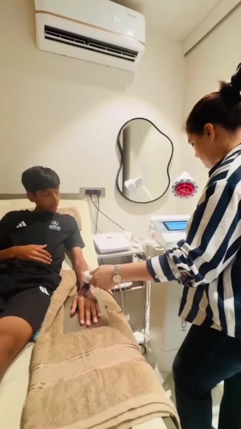 Seated boy rests his arm on a towel while a therapist treats his forearm