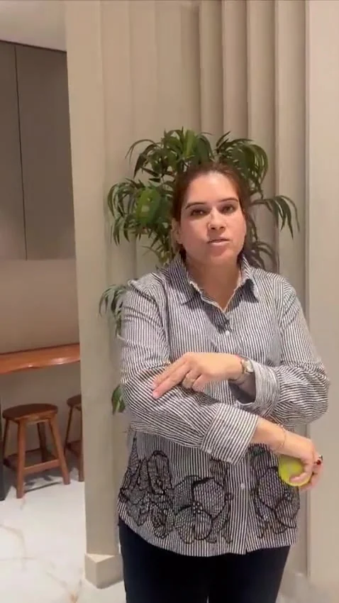 Woman holds a yellow ball in one hand and points toward her forearm while speaking.