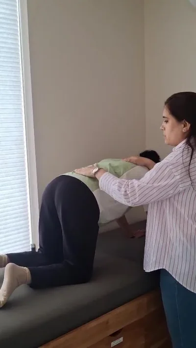 Physiotherapist resting both hands across the lower back of a patient in four-point kneeling on a treatment couch.